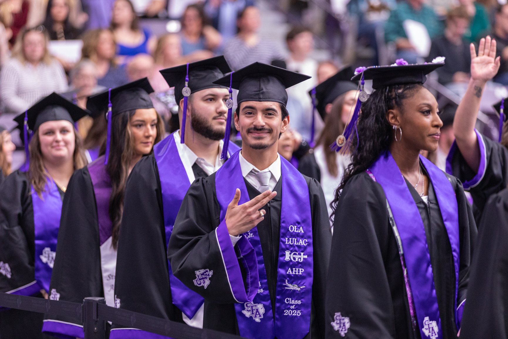 Luciano Hinojosa Jr., an Aviation Science major, gives the Axe em, Jacks hand sign during the December commencement ceremony at Stephen F. Austin State University's Johnson Coliseum. Series produced for Stephen F. Austin State University social media, 2025